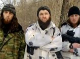 Умаров говорит на фоне заснеженного леса, рядом с ним стоят двое молодых людей, один из которых держит автомат Калашникова с подствольным гранатометом