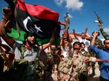 К толпе бойцов вооруженных формирований присоединились проезжавшие мимо на машинах местные жители, которые стали размахивать оказавшимися у них под рукой новыми ливийскими флагами