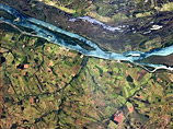 Снимок ярко-голубой реки в окружении невысоких фермерских строений и обширных полей в Бразилии