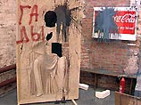 На ней были представлены экспонаты, вызвавшие возмущение у многих верующих, в частности, икона Спасителя на фоне рекламы "Coca-Cola" с надписью "Сие есть кровь моя", а также фигура святого с вырезанным ликом, куда каждый желающий мог подставить голову На ней были представлены экспонаты, вызвавшие возмущение у многих верующих, в частности, икона Спасителя на фоне рекламы "Coca-Cola" с надписью "Сие есть кровь моя", а также фигура святого с вырезанным ликом, куда каждый желающий мог подставить голову