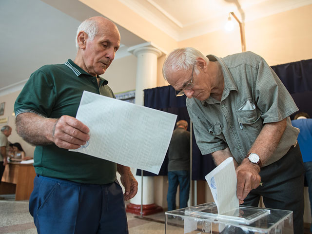 Мужчины опускают бюллетени в урну для голосования на выборах главы Абхазии на избирательном участке в Сухуми