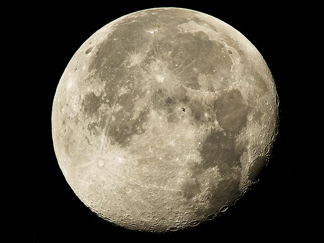 На сайте NASA в разделе "Фото дня" опубликовано изображение Международной космической станции, проходящей на фоне полной луны. Силуэт МКС, крошечный по сравнению с огромным лунным диском, виден ближе к центру кадра
