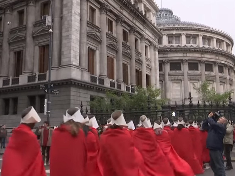 В среду, 8 августа, сотни женщин в красных плащах и белых головных уборах, таких же, как носят служанки в сериале-антиутопии "Рассказ служанки", вышли на улицы столицы Аргентины
